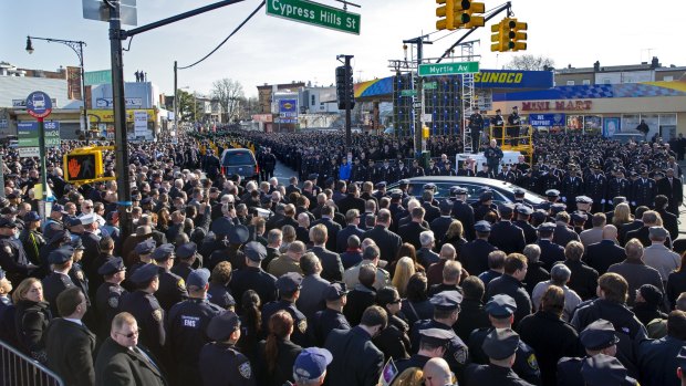 Thousands of police officers and others stand at attention as a hearse carrying New York City police officer Rafael Ramos passes by after his funeral.