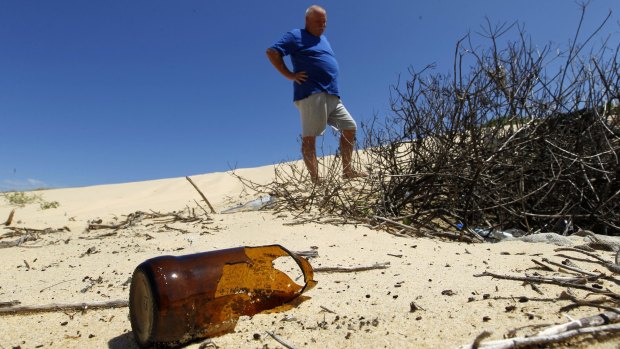 Tony McEnally, treasure of Belmont Wetlands State Park Trust, examines rubbish in the dunes on Redhead Beach in 2015. The trust campaigned to implement a permit for vehicle access.