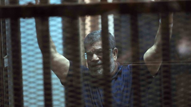 Sentenced to death: Ousted Egyptian President Mohammed Morsi raises his hands as he sits behind glass in a courtroom.