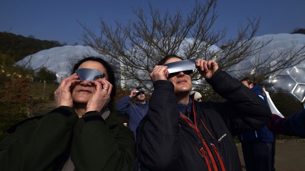 People watch as a solar eclipse begins over the Eden Project near St Austell in Cornwall.