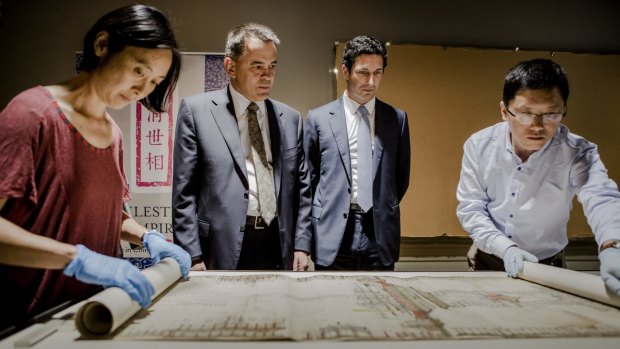 The National Library of Australia's preservation manager Lisa Jeong-Reuss and National Library of China Conservator Zhu Zhenbin
unfurl the plan of the Forbidden City Palace at the launch of "Celestial Empire: Life in China 1644-191", while MLA Chris Bourke and NLA council chairman Ryan Stokes look on.