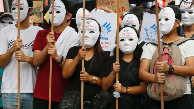 Masked protesters display placards as as they call on the Philippine government to end extra-judicial killings of accused drug users and dealers last year.