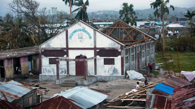 Residents stand near a church that had its roof ripped away by Hurricane Matthew in Les Cayes, Haiti.