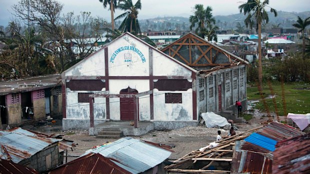 Residents stand near a church that had its roof ripped away by Hurricane Matthew in Les Cayes, Haiti.