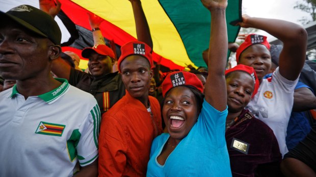 Protesters raise their fists under a large national flag, at a demonstration of tens of thousands at Zimbabwe Grounds in Harare.