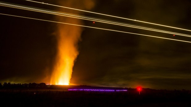 Planes continue to land  while a fire near the Canberra Concrete Recyclers on Pialligo Avenue blazes away on Thursday night.