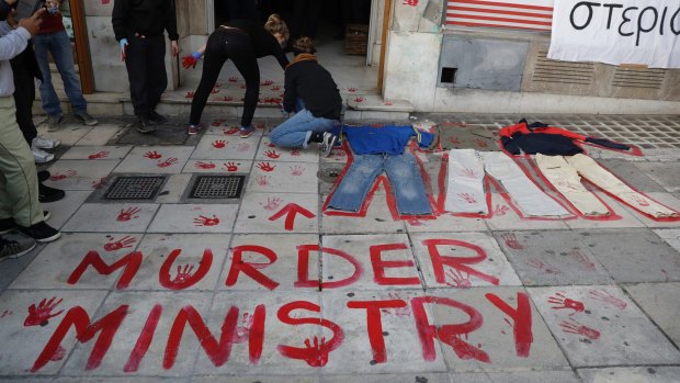 Demonstrators use red paint during a rally outside the Migration Ministry in Athens, to protest against camp conditions after the deaths of five migrants.