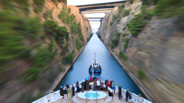 Tourists on the bow of a small cruise ship being pulled by a tug, early morning transit of Corinth Canal, Greece.
