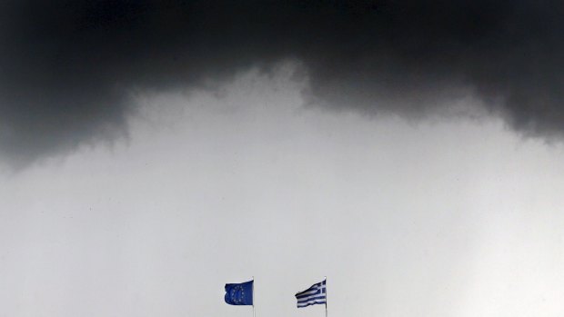 Greek and European Union flags flutter under storm clouds in Athens.