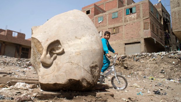 A boy rides his bicycle past the recently discovered statue in a Cairo slum.