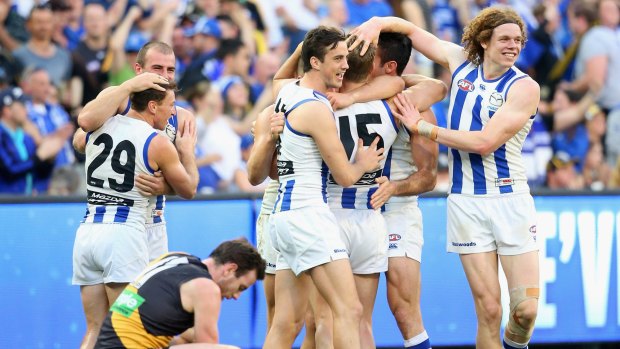 Roo huddle: North Melbourne players celebrate while Tiger Jake Batchelor sinks to the ground.