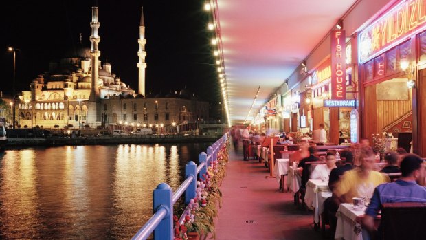 Tourists dining along Galata Bridge at night in Istanbul.