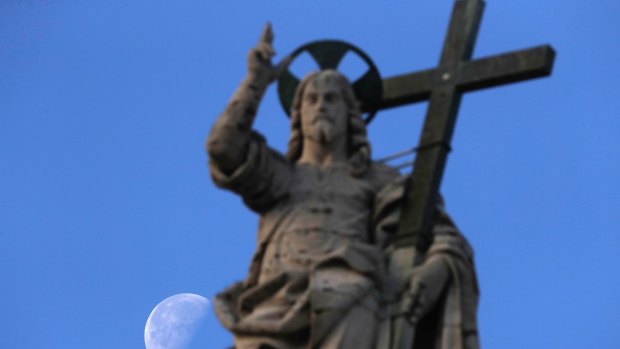 The moon sets behind the statue of Jesus.