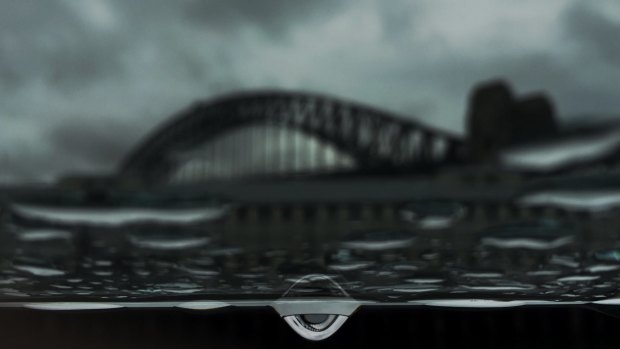 An image of Sydney Harbour Bridge is refracted in a raindrop on a window.  