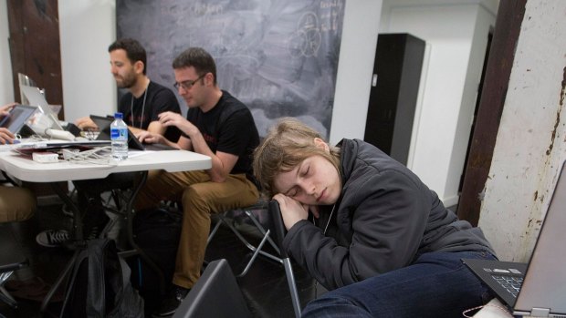 Sarah Erlington sleeps after working on her project all night at the NAB Hackathon in Sydney in November, while Juliius Neggo (left) and Justin Liang chew over ideas.