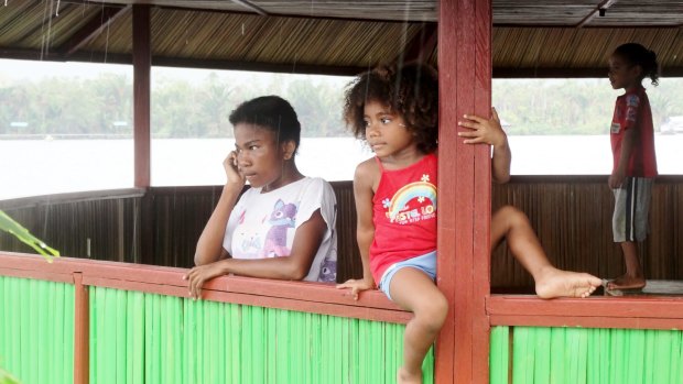 Children watch wooden boats take the group away from a rainy Assey Island in the middle of Lake Sentani, Jayapura, West Papua.