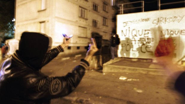 Youths gesture next to a wall with graffiti  that reads "F--- the police, Sarkozy resign", in the Renault housing complex of Les Mureaux, north-west of Paris, during the riots of 2005.