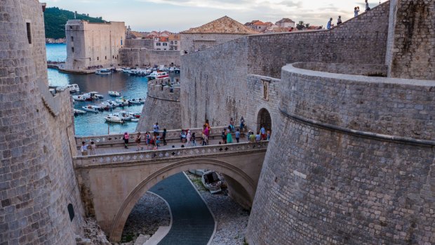 People walking across a small bridge to visit Dubrovnik city walls.