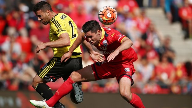 Dylan McGowan of Adelaide United clears the ball in front of Manny Muscat of Wellington Phoenix.