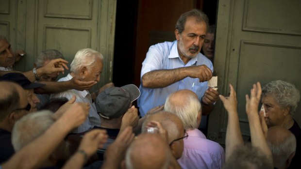 A bank employee distributes tags with queue positions to pensioners outside the national bank in Athens.