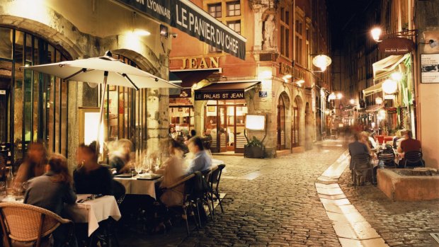 Lyon, People dining along cobbled street at night.