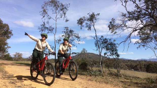 ACT Parks and Conservation volunteer programs manager Alison McLeod and visitor experience manager Jasmine Foxlee riding through Canberra's nature parks on electric mountain bikes.