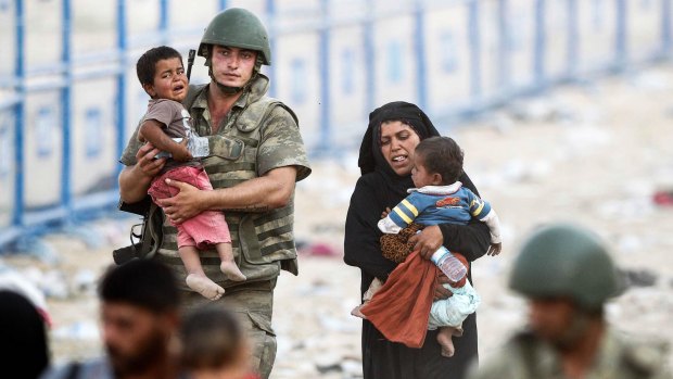 A Turkish soldier carries a Syrian child as they walk to cross into Turkey at Akcakale border gate on Monday.