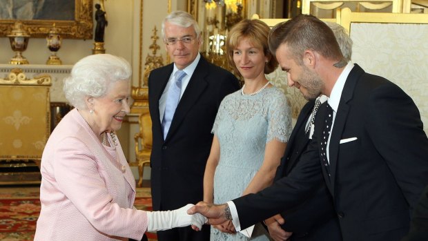 Britain's Queen Elizabeth II (L) shakes hands with former England footballer David Beckham (R) as former prime minister John Major (2L) looks on during a reception for The Queen's Young Leaders at Buckingham Palace in London on June 22, 2015. 
