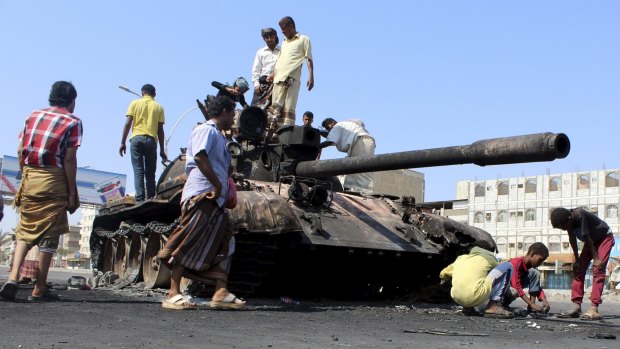 People gather near a tank burnt during clashes on a street in Yemen's southern port city of Aden March 29, 2015. 