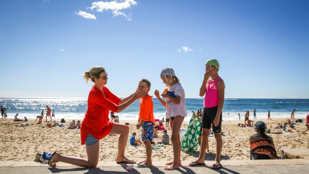 Kate Swift and her three children Carter, 5, Willow, 7, and Finn, 9, apply sunscreen at Coogee Beach.