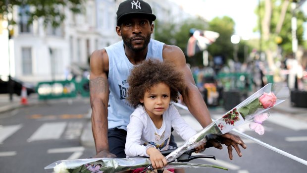 A young girl carries a flower to a memorial site near Grenfell Tower.