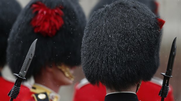 Soldiers stand in heavy rain at Buckingham Palace.