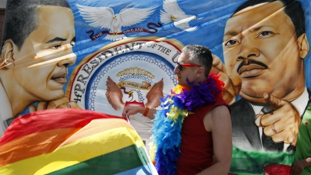 A gay rights protester stands in front of a mural featuring Martin Luther King.