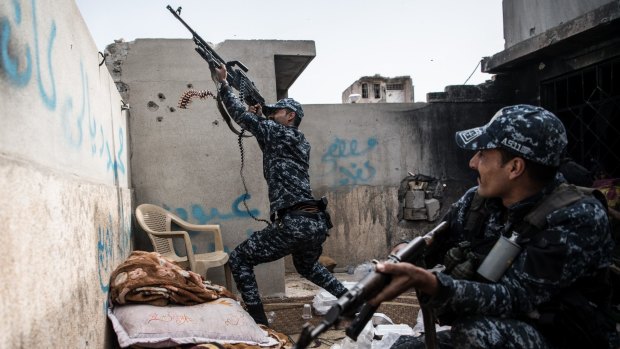 An Iraqi policeman fires a machine gun at an Islamic State position on a nearby rooftop.