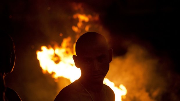 A Hindu man stands beside a burning pyre during the cremation of a relative, a victim of the April 25 earthquake, at the Pashupatinath temple on the banks of the Bagmati River in Kathmandu, Nepal, on Friday, 