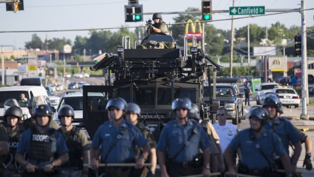 Clash: Riot police stand guard as demonstrators protest in Ferguson in August.
