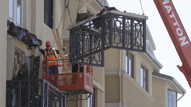 Workers with remove part of a fourth floor balcony that fell onto the balcony below.
