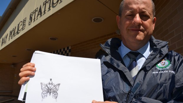 Detective Inspector Kevin McNeil with a copy of the butterfly pendant police hope will identify a woman found dead in Tathra on Wednesday.