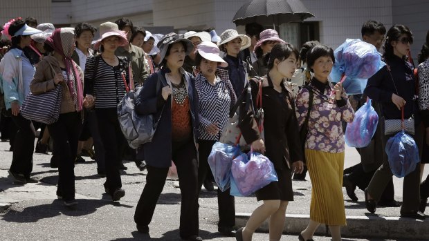 Doing their duty: North Korean women carrying decorative flowers walk from the Kim Il Sung Square on Sunday after rehearsing for a parade.