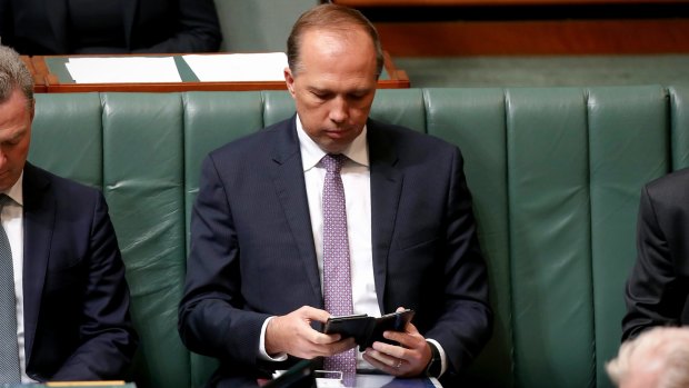 Minister for Immigration and Border Protection Peter Dutton checks his phone. His number was among those leaked.
