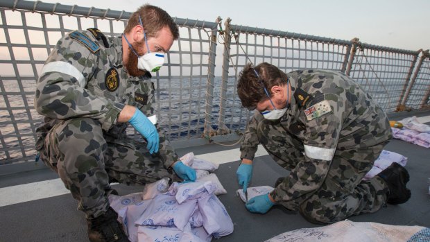Able Seaman Marine Technicians Bryce Williams (left) and Ryan Kimber remove the outer packing from seized parcels of heroin on the flight deck of HMAS Warramunga on January 24.