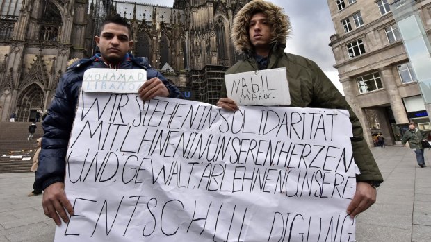 Mohamad of Lebanon, left, and Nabil of Morocco hold a banner in front of the Cologne cathedral to apologise for other migrants' crimes. The sign reads "we stand in solidarity in our hearts with you, we refuse  violence and hope you accept our apologize". 
