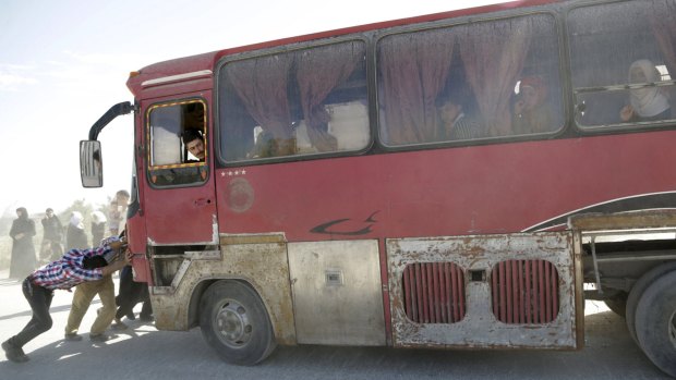 Men push a bus carrying civilians fleeing the north-western city of Ariha.