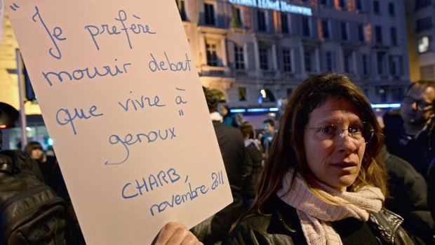 A woman holds a placard reading in French "I'd rather die standing than to live on my knees-Charb" during a gathering in Marseille, on January 7, 2015.