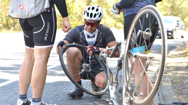 Cholo Santos fixes his punctured tyre during a stop the tacks protest ride in Kew. 