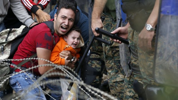 A migrant holding a boy reacts as they are stuck between Macedonian riot police and fellow migrants during a clash in northern Greece.