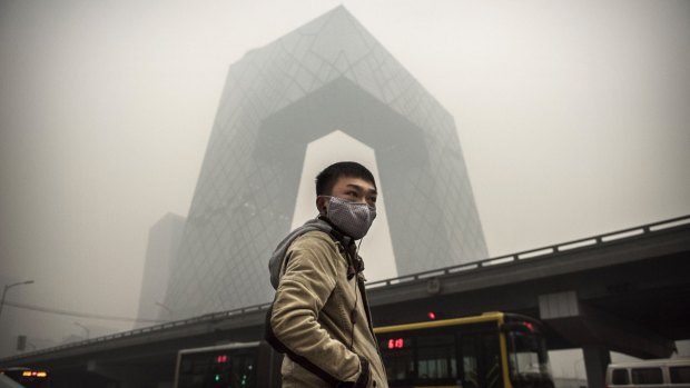 A Chinese man wears a mask as he waits to cross the road near the CCTV building during heavy smog in 2014. 