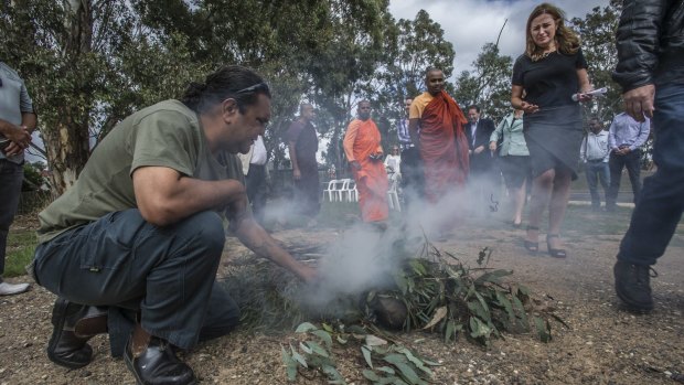 Ranger Adrian Brown conducts the smoking ceremony in Kambah as Housing Minister Yvette Berry walks past.