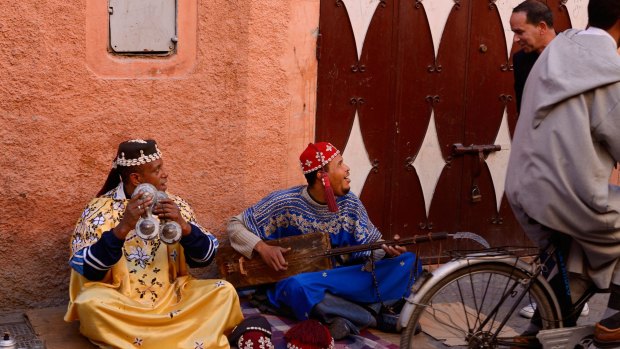 Gnawa street musicians playing hajhuj and krakeb in Marrakech talking to a passerby.