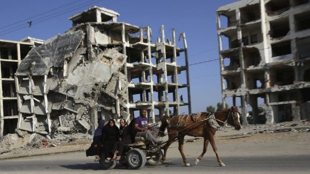 A Palestinian family rides a horse cart as they pass apartment buildings that were destroyed in the most recent Israel-Hamas war, in Gaza Strip.